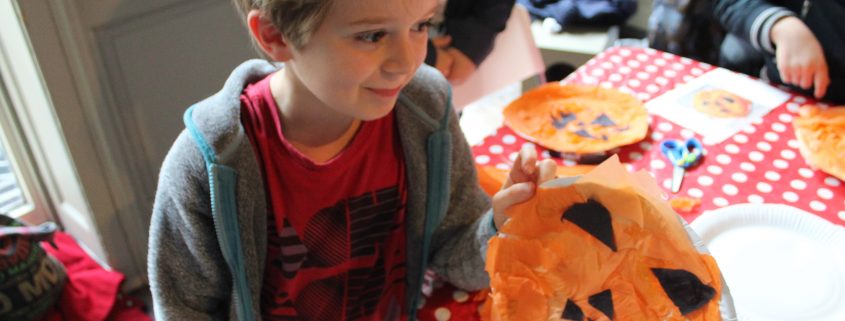 Child holding up pumpkin face craft on paper plate